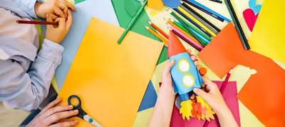 Manos de un joven recortando y pegando papel para armar una manualidad sobre una mesa