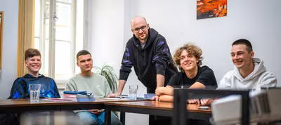 Estudiantes trabajando en equipo alrededor de una mesa mientras su maestro los guía con preguntas