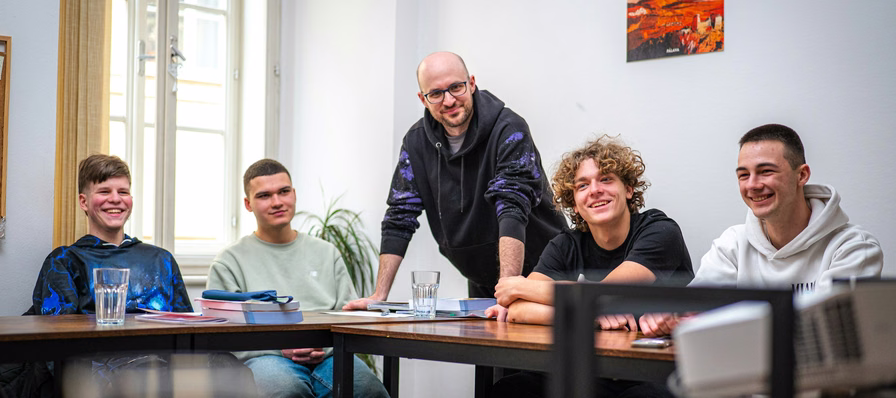 Estudiantes trabajando en equipo alrededor de una mesa mientras su maestro los guía con preguntas